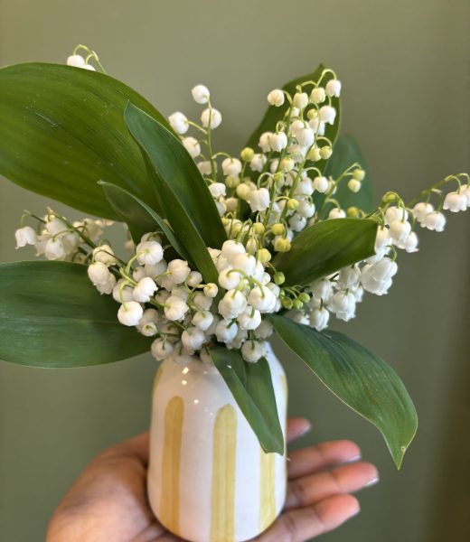 Bouquet de muguet du 1er mai dans un petit vase artisanal rayé jaune et blanc tenu dans une main - Flormandise Vernioz